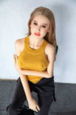 A woman in a yellow tank top and black pants sits on a chair.