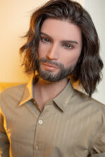 A lifelike male doll with long dark hair and a beard, wearing a tan button-up shirt.
