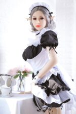 A doll with elf ears in a black and white maid outfit stands beside a table with tea items and flowers.