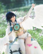 A cosplayer in a white and gold angelic costume with large wings sits in a field of flowers.